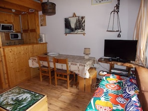 A cozy room with a wooden dining table, chairs, a television, and a bed with a colorful blanket. - Perfectly located apartment - 4 guests (Pralognan-la-Vanoise)