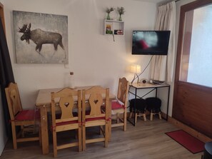 A cozy room with a wooden dining table, chairs, a television, and a painting of a moose. - Studio-cabin near slopes - 4 guests (Pralognan-la-Vanoise)