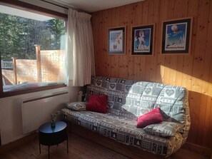 A cozy room with a patterned sofa, a small table with a vase, and framed pictures on the wall. - Studio-cabin near slopes - 4 guests (Pralognan-la-Vanoise)