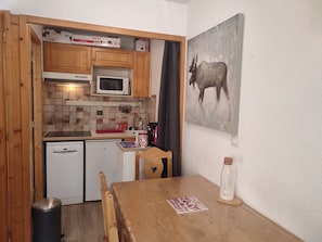 A compact kitchen with wooden cabinets, a microwave, a small refrigerator, and a dining table with chairs. - Studio-cabin near slopes - 4 guests (Pralognan-la-Vanoise)