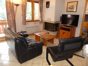 Een woonkamer met een bank, een fauteuil, een salontafel, een open haard en een televisie.