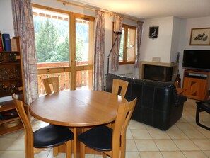 A dining area with a wooden table and chairs, a sofa, a television, and a fireplace. - Comfortable apartment - 7 guests (Pralognan-la-Vanoise)