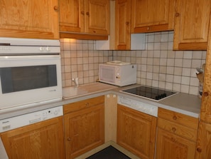 A kitchen with wooden cabinets, a white dishwasher, a microwave, and a stove. - Comfortable apartment - 7 guests (Pralognan-la-Vanoise)