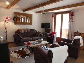 A cozy living room with a leather sofa, a wooden coffee table, and a television. - Spacious chalet - 4 guests (Pralognan-la-Vanoise)