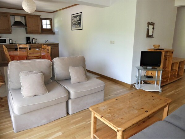 Een woonkamer met een zithoek, een houten salontafel en een tv op een meubel.