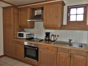 A kitchen with wooden cabinets, a microwave, a toaster, a coffee maker, and a sink. - Cozy three-room near slopes - 6 guests (Pralognan-la-Vanoise)