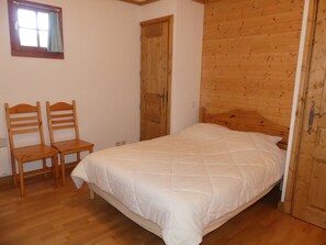 A bedroom with a wooden bed, two wooden chairs, a wooden wardrobe, and a window with curtains. - Cozy three-room near slopes - 6 guests (Pralognan-la-Vanoise)