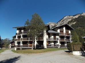 A multi-story building with balconies, a tree in front, and a mountain in the background. - Duplex at the foot of the slopes - 4 guests (Pralognan-la-Vanoise)