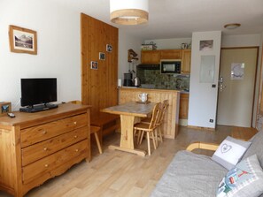 A compact living space with a wooden dining table, a sofa, a TV, and a kitchenette. - Apartment in exclusive area - 4 guests (Pralognan-la-Vanoise)
