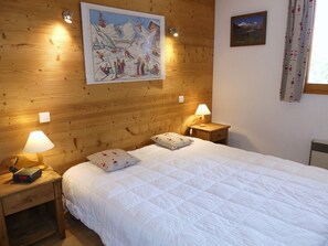 A hotel room with a wooden wall, a bed with white bedding, two bedside lamps, and a ski-themed painting above the bed. - Apartment in exclusive area - 4 guests (Pralognan-la-Vanoise)