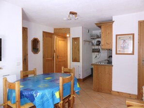 A dining area with a table and chairs, a kitchen with wooden cabinets, and a tiled floor. - Cozy mountain-style apartment - 4 guests (Pralognan-la-Vanoise)