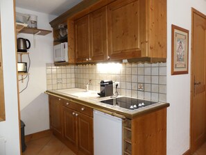 A compact kitchen with wooden cabinets, a white countertop, a built-in microwave, and a coffee maker. - Cozy mountain-style apartment - 4 guests (Pralognan-la-Vanoise)