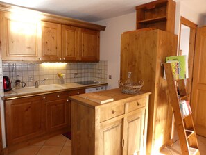 Eine Küche mit Holzschränken, einer gefliesten Spritzschutzwand, einem Spülbecken, einer Kaffeemaschine und einer an der Wand stehenden Leiter.