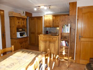 Eine Küche mit Holzausstattung, einer Mikrowelle, einer gefliesten Spritzschutzwand und einem Esstisch mit Stühlen.
