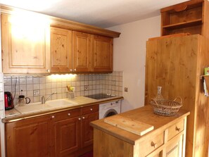 Een keuken met houten kastjes, een spoelbak, een fornuis en een wasmachine.