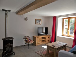 A living room with a television, a wooden cabinet, a wicker chair, a small table, and a large window with curtains. - Renovated house at the slopes - 5 guests (Pralognan-la-Vanoise)