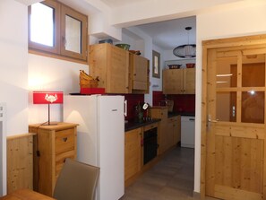 A compact kitchen with wooden cabinets, a refrigerator, a sink, and a dining area with a table and chairs. - Apartment with terrace - 6 guests (Pralognan-la-Vanoise)