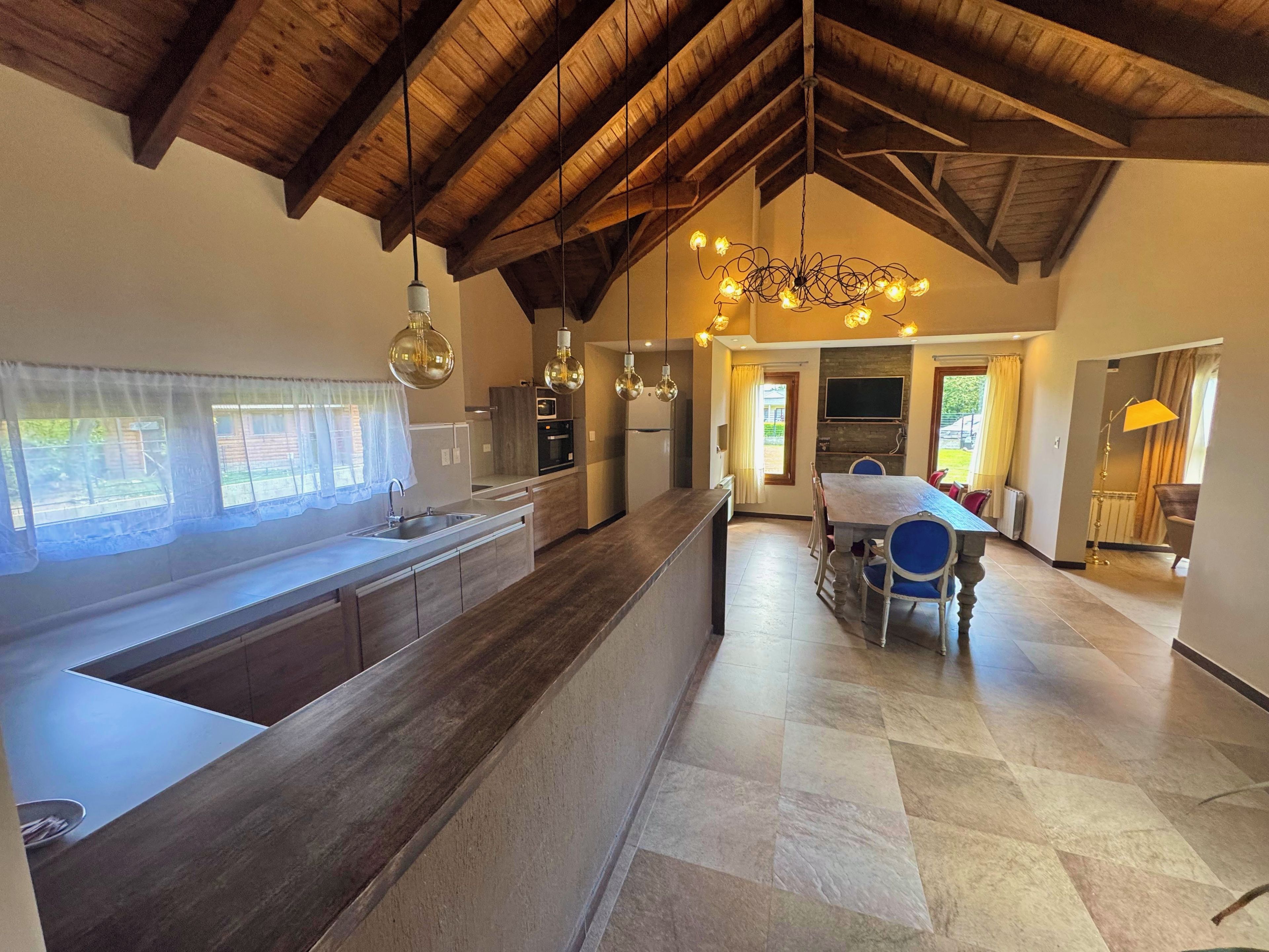 A spacious kitchen with a large island, wooden ceiling beams, and pendant lighting.