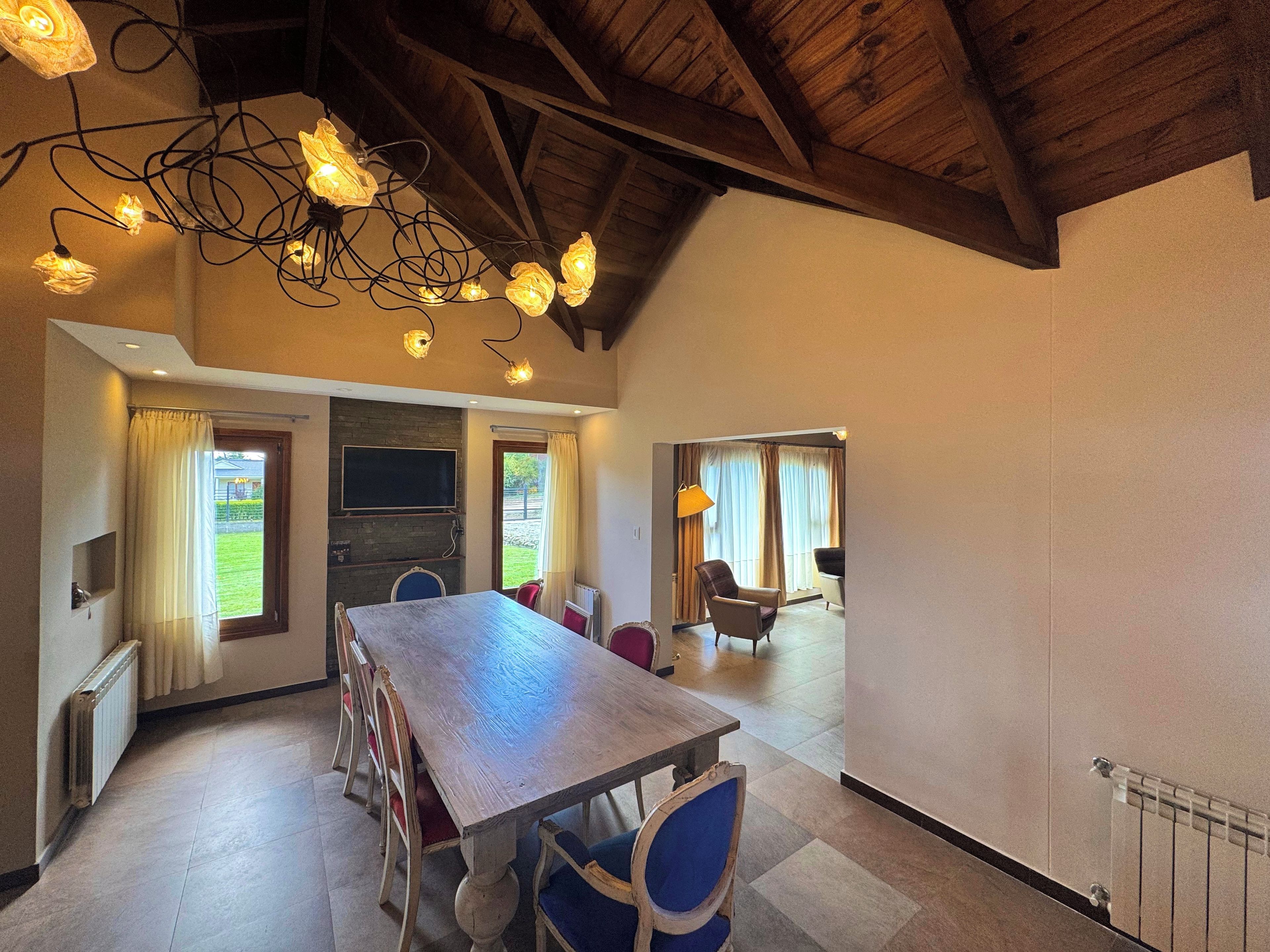 Una habitación amplia con una mesa y sillas de madera, chimenea y vistas al exterior.