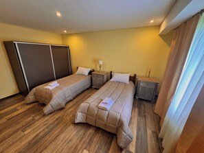 Une chambre d’hôtel avec deux lits, un plancher en bois, une armoire, des tables de chevet avec des lampes et une fenêtre avec des rideaux.