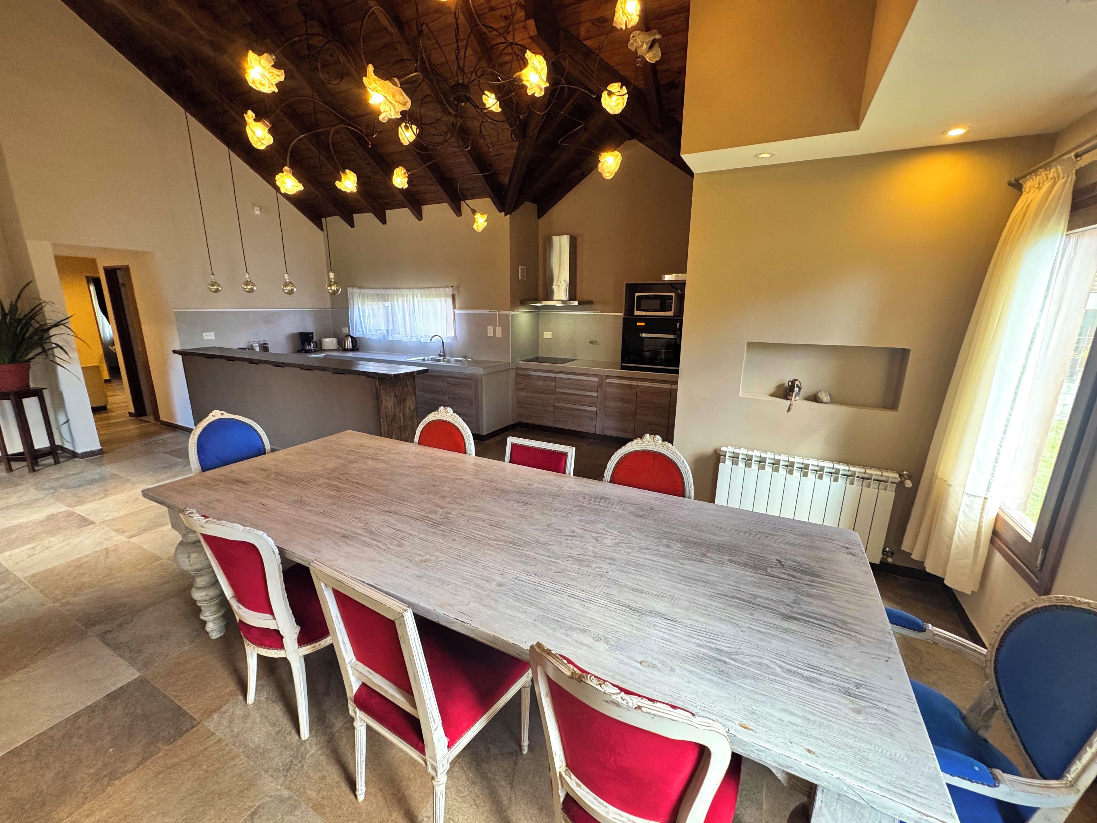A dining area with a long wooden table and red upholstered chairs.