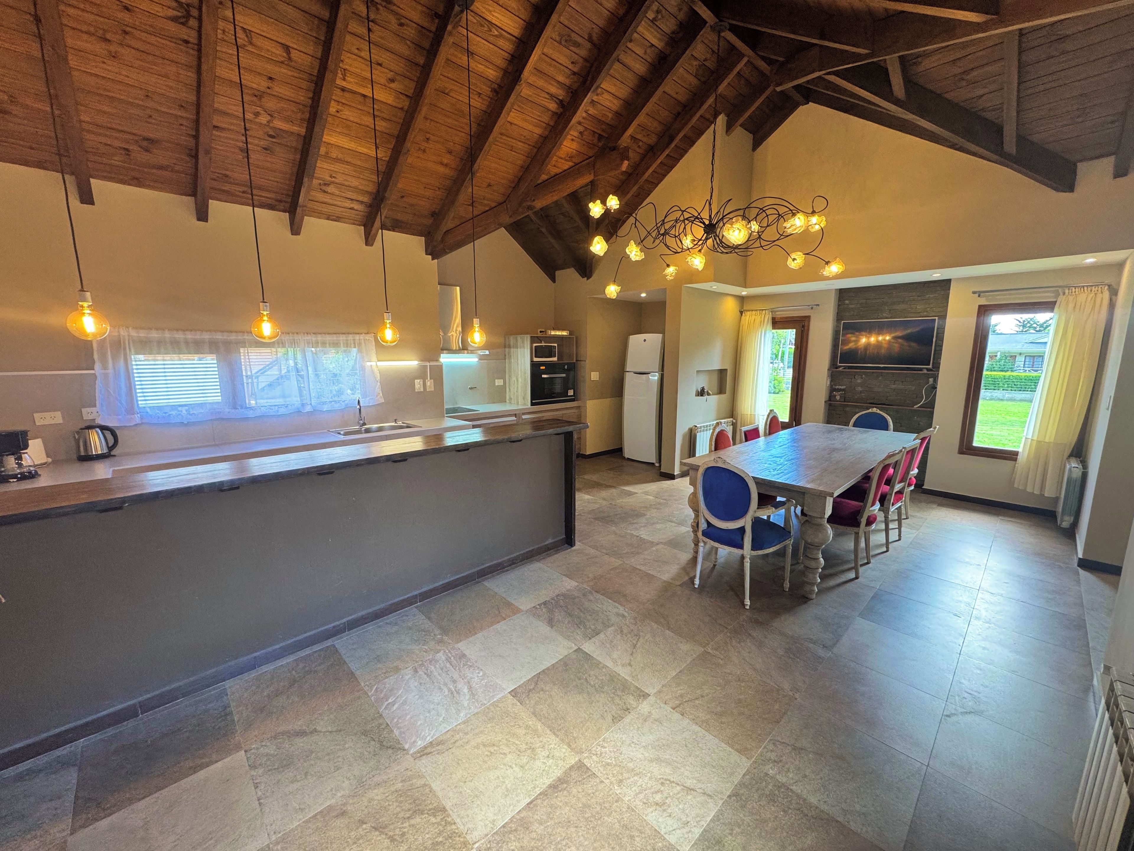A modern kitchen with a central island, a dining area with a table and chairs, and a view of the outdoors through a window.