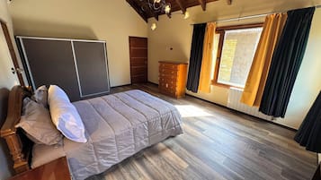 A bedroom with a bed, wooden headboard, a dresser, a wardrobe, and a window with curtains.