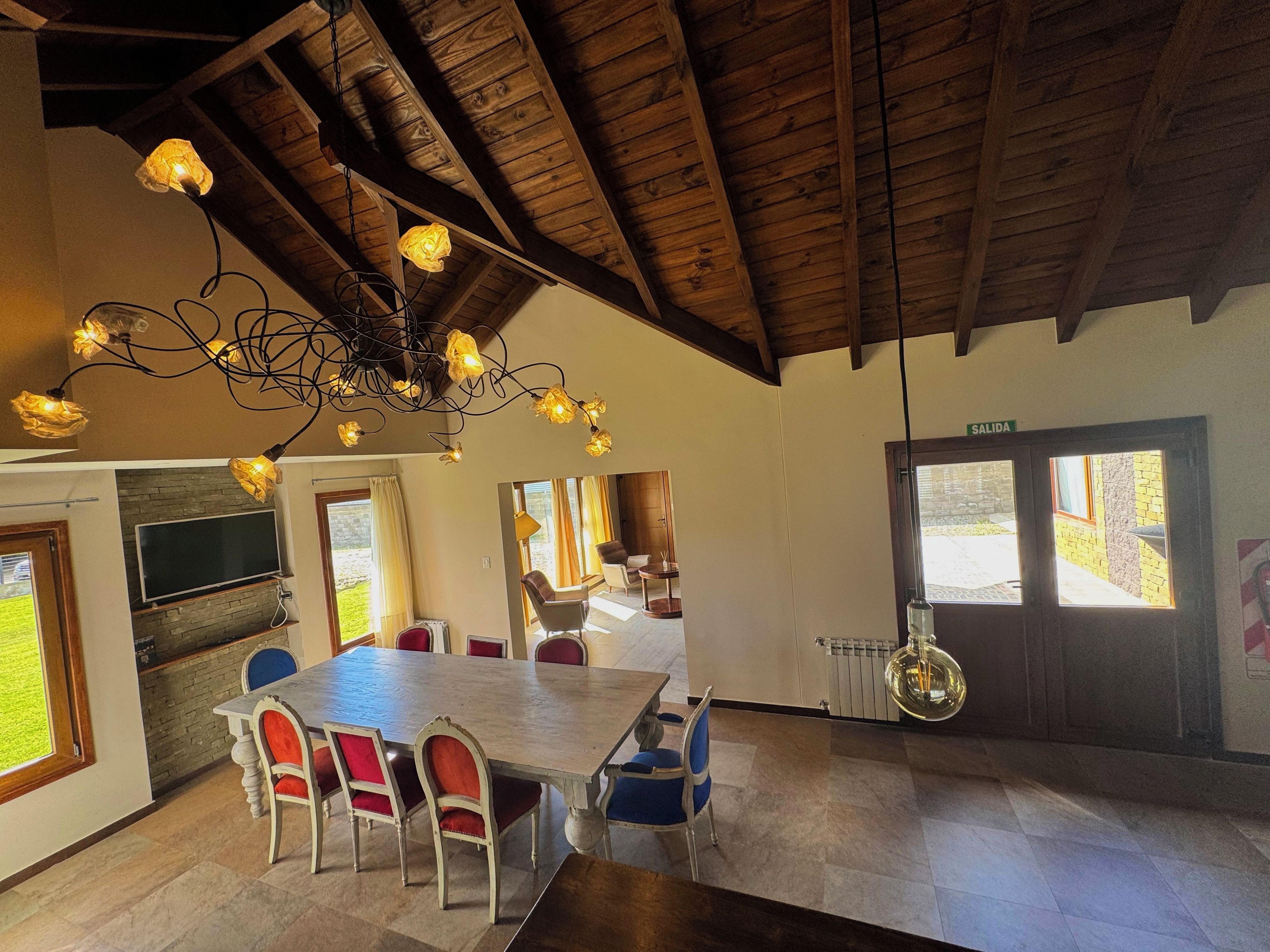 Un espace repas doté d’un plafond en bois, d’un lustre et d’une grande table entourée de chaises.