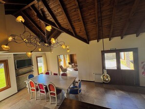 A dining area with a wooden ceiling, a chandelier, and a large table with chairs.