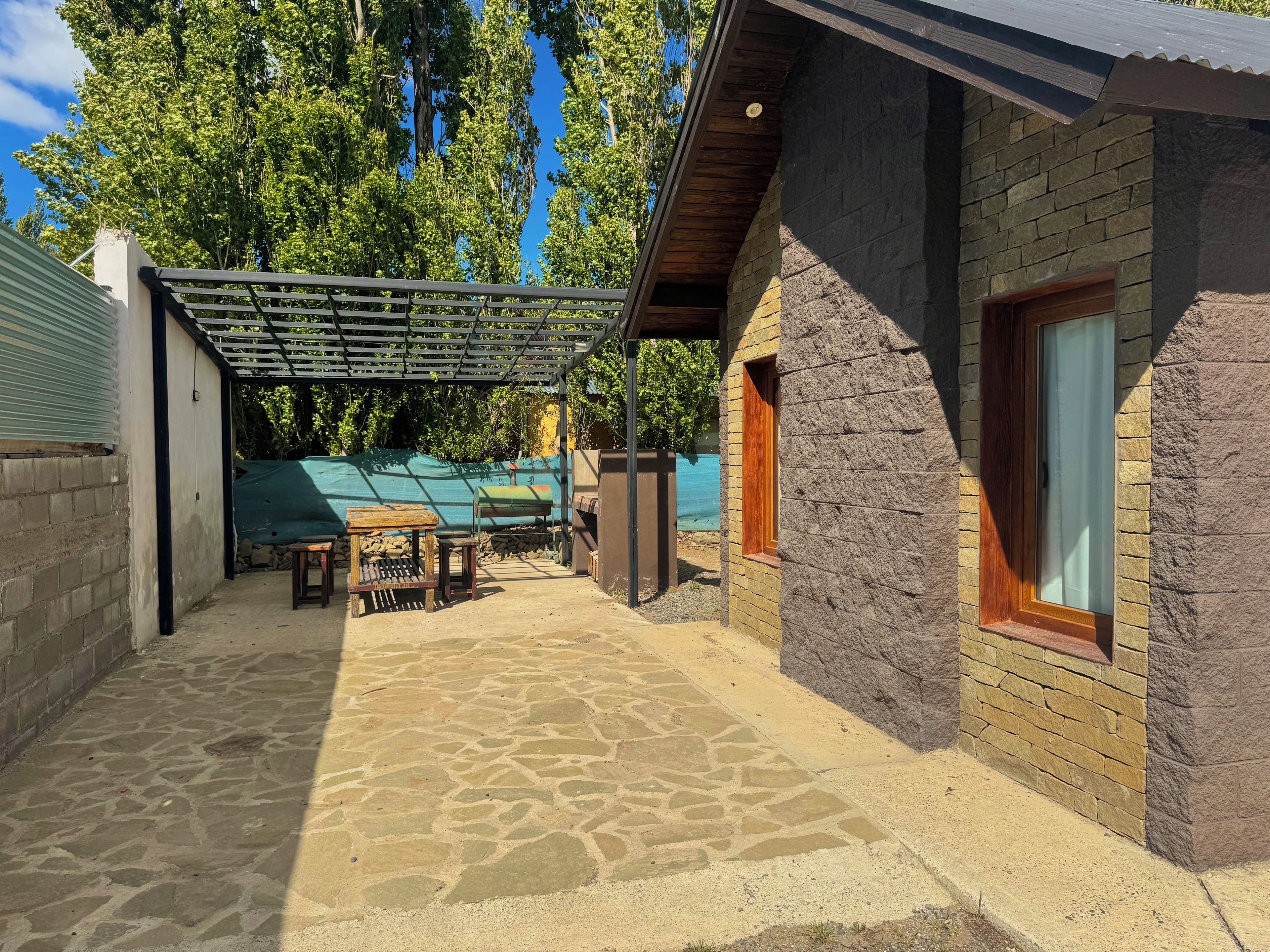 Un espace extérieur abrité, doté d’un sol en pierre, d’une table en bois et d’une bâche verte.