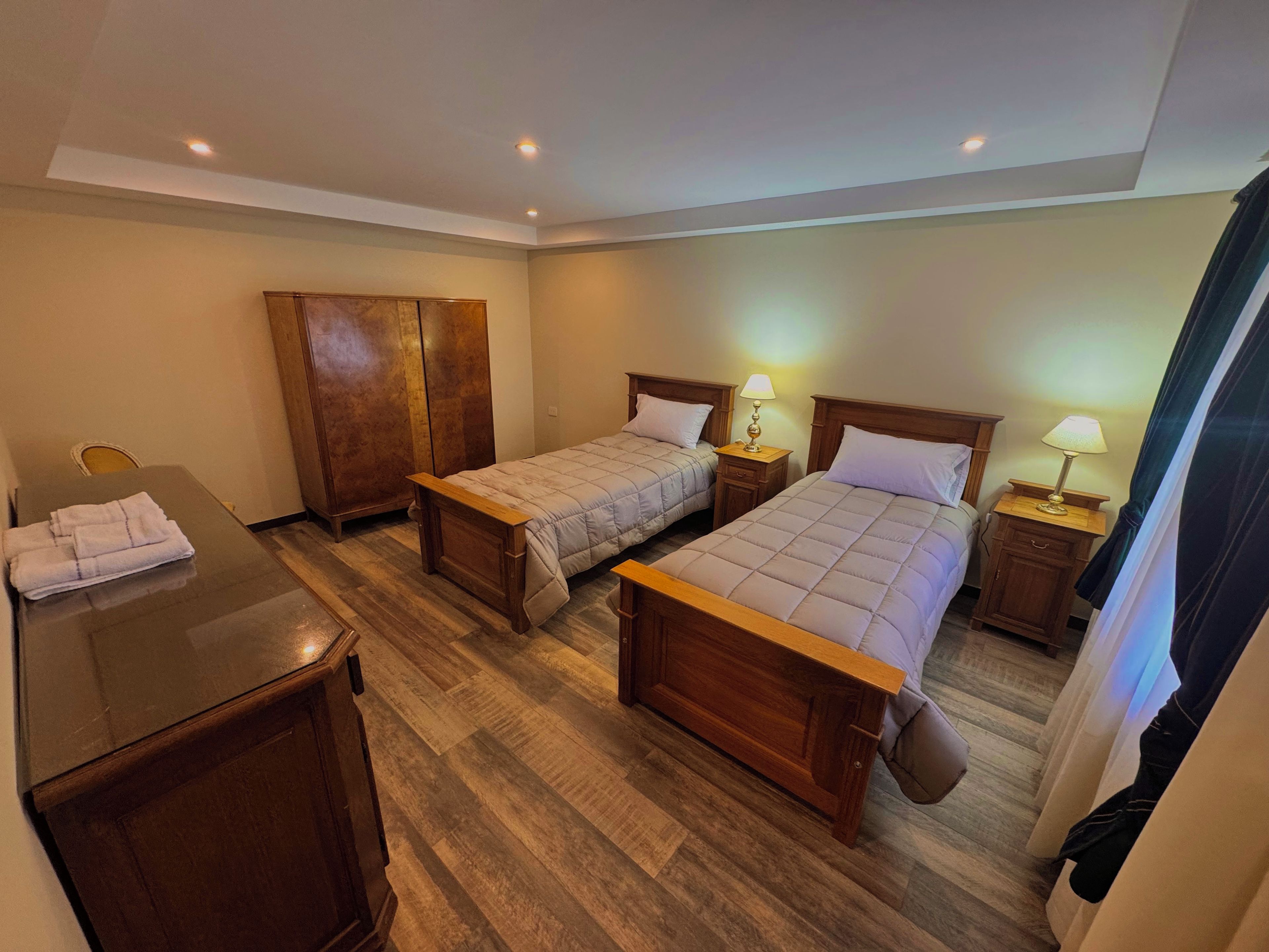 A hotel room with two beds, a wooden desk, and a chair.