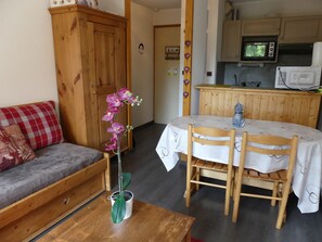 A cozy living area with a wooden sofa, a dining table with chairs, and a kitchen area with wooden cabinets and appliances. - Sunny apartment - 4 guests (Pralognan-la-Vanoise)