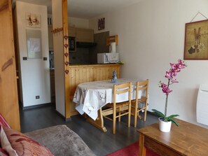 A cozy dining area with a wooden table and chairs, a potted orchid, and a kitchen in the background. - Sunny apartment - 4 guests (Pralognan-la-Vanoise)