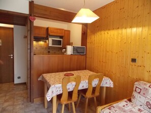 Een compacte keuken met houten kastjes, een magnetron en een tafel met stoelen.