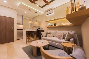 A modern living room with a sofa, coffee table, and a kitchen area in the background. - Lux 1BR  Ocean-View Pool  w/Habitas Beach Club (Tulum)