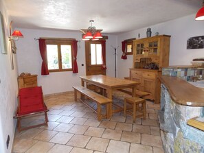 Une cuisine avec une table en bois, des bancs, un buffet en bois et une chaise rouge.