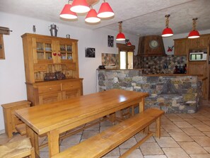 A wooden dining table with benches, a stone wall, and red pendant lights in a kitchen. - Ground floor chalet, 6 guests - Pralognan-la-Vanoise (Pralognan-la-Vanoise)