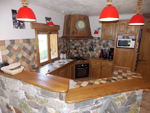 Une cuisine dotée d’un îlot central en pierre, de meubles de rangement en bois, d’un four à micro-ondes et de luminaires suspendus rouges.