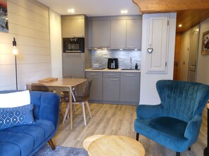 En kompakt opholdsstue med spiseplads, et tekøkken og en siddeplads med en blå sofa og lænestol.