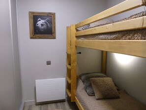 En køjeseng med et billedrammet billede over, en hvid radiator nedenunder og et lille hyldesæt til højre.