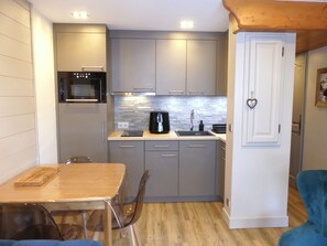 A compact kitchen with a microwave, coffee maker, and a small sink. There is a dining table with chairs and a blue sofa in the living area. - Charming apartment - 4 guests (Pralognan-la-Vanoise)