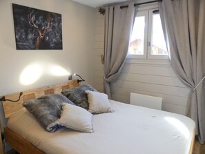 A bedroom with a wooden headboard, a bed with white and grey pillows, a nightstand with a lamp, and a window with curtains. - Charming apartment - 4 guests (Pralognan-la-Vanoise)