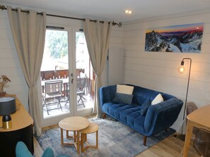 A cozy living room with a blue sofa, a small round table, and a view through a glass door to an outdoor area. - Charming apartment - 4 guests (Pralognan-la-Vanoise)