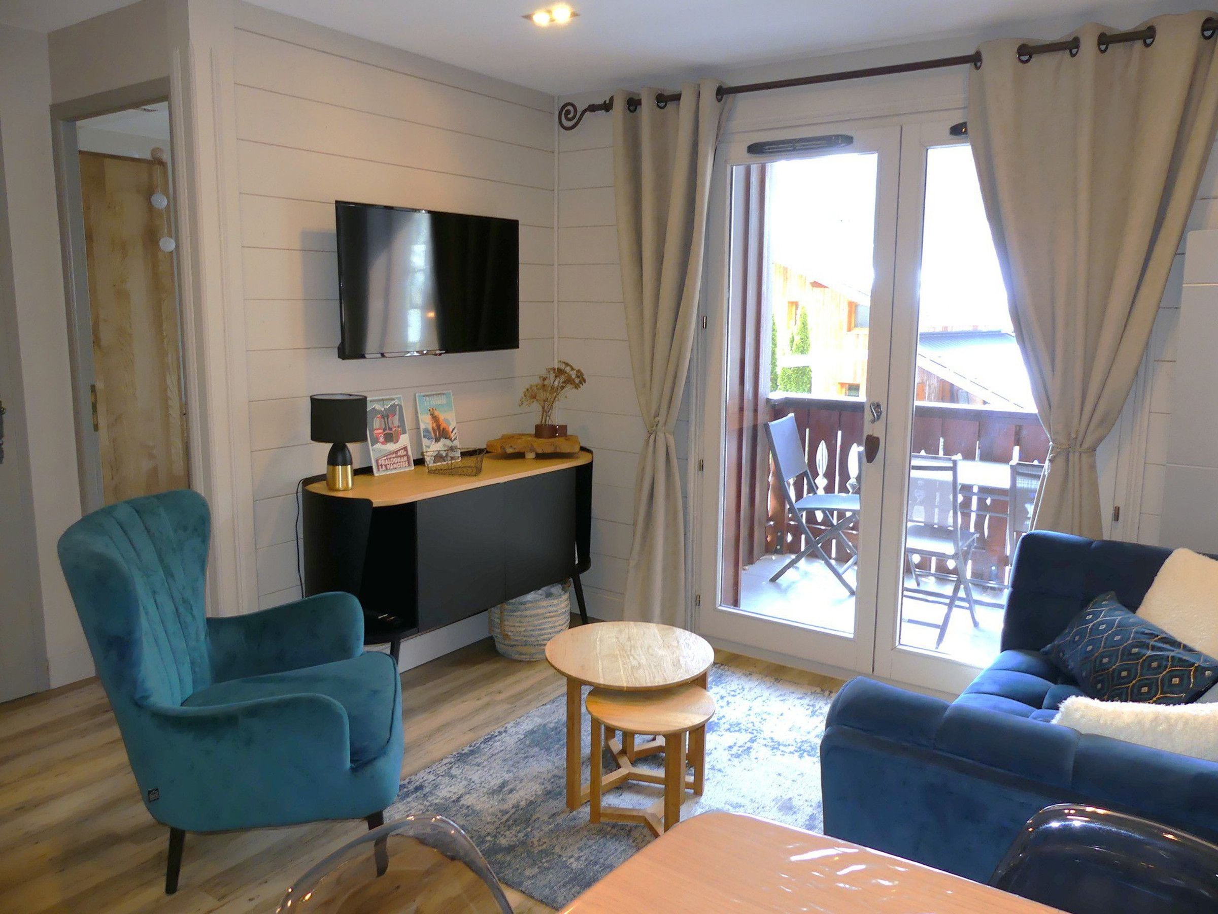 A living room with a TV, a desk, a blue sofa, and a dining area with chairs.