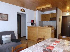 A cozy room with a wooden table, a sofa, and a kitchen area with wooden cabinets and a microwave. - Comfortable apartment near the Nordic area - 6 guests (Pralognan-la-Vanoise)