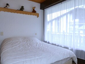 A bedroom with a bed, a window with curtains, and a shelf with decorative items. - Comfortable apartment near the Nordic area - 6 guests (Pralognan-la-Vanoise)