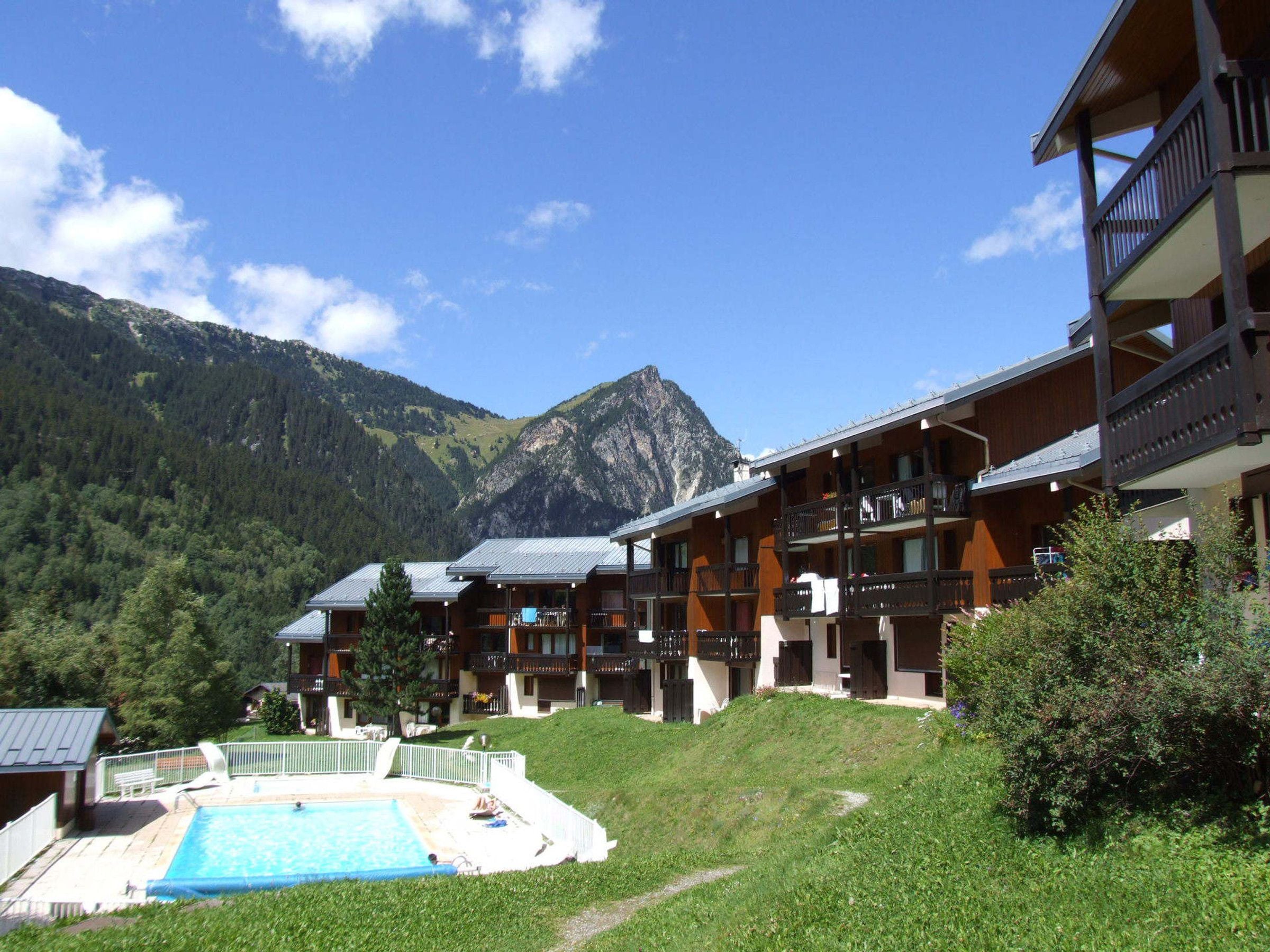 A hotel with multiple balconies, a swimming pool, and a mountainous backdrop.