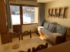 A cozy room with a wooden sofa, a dining table with chairs, and a window with curtains. - Charming apartment without equipment - 4 guests (Pralognan-la-Vanoise)