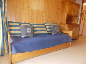 A wooden bed with blue bedding and patterned pillows, a wooden wardrobe, and a wooden bench. - Sunny apartment - 4 guests (Pralognan-la-Vanoise)
