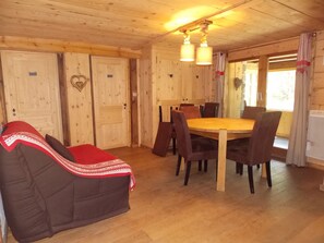 A wooden interior with a round table and chairs, a sofa with a red blanket, and a door with a heart-shaped decoration. - Chalet, pets allowed - 8 guests in quiet area (Pralognan-la-Vanoise)